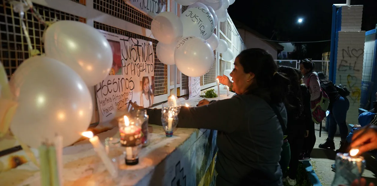 Personas prenden velas frente a carteles de reclamo de justicia y globos blancos colocados en una reja.