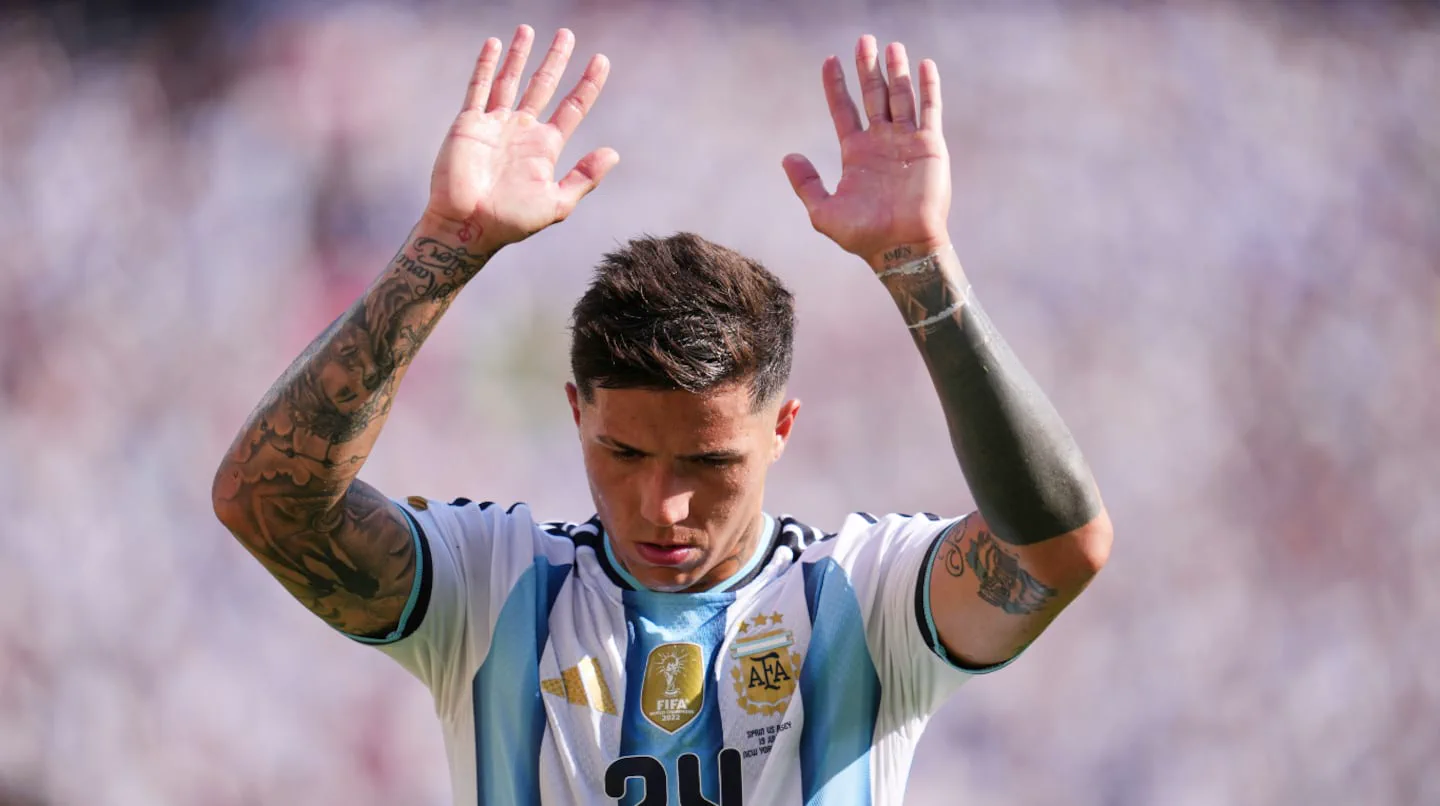 Enzo Fernández con la camiseta de la selección argentina mirando hacia abajo y levantando las dos manos.