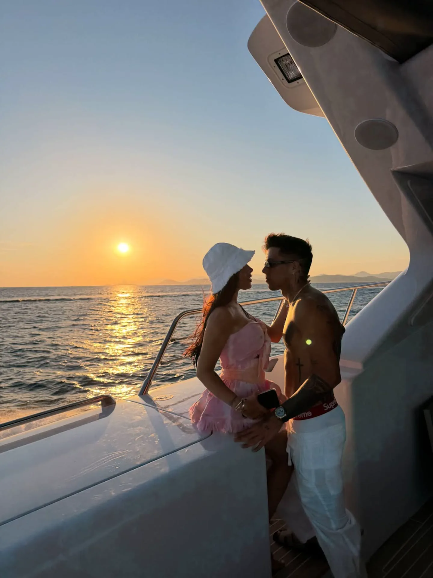 Una pareja parada en la cubierta de un barco mirándose de cerca durante el atardecer sobre el mar.