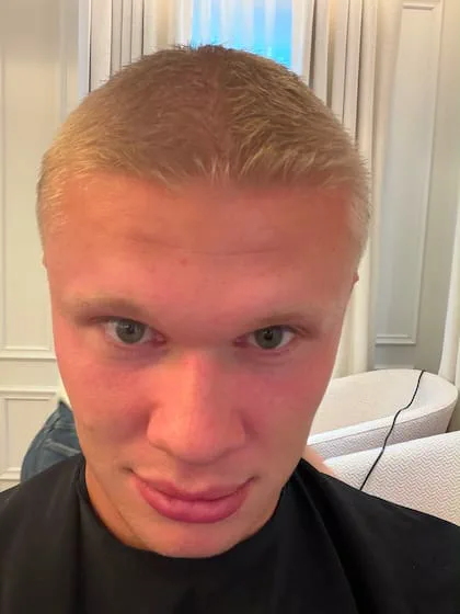 Erling Haaland en primer plano con el pelo rubio muy corto y una capa de peluquería puesta.