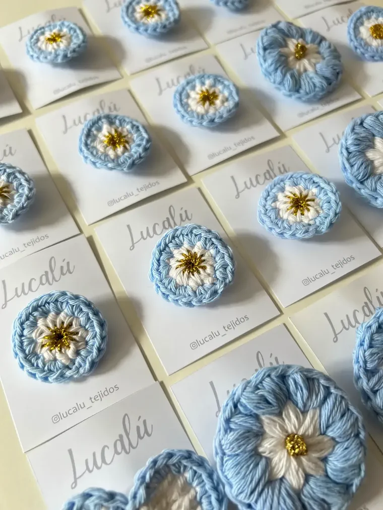 Varias escarapelas argentinas tejidas al crochet sobre tarjetas de presentación blancas.
