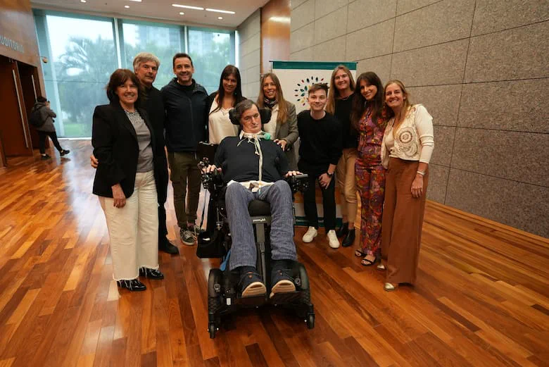Esteban Bullrich en silla de ruedas posa junto a un grupo de personas en un salón con piso de madera.