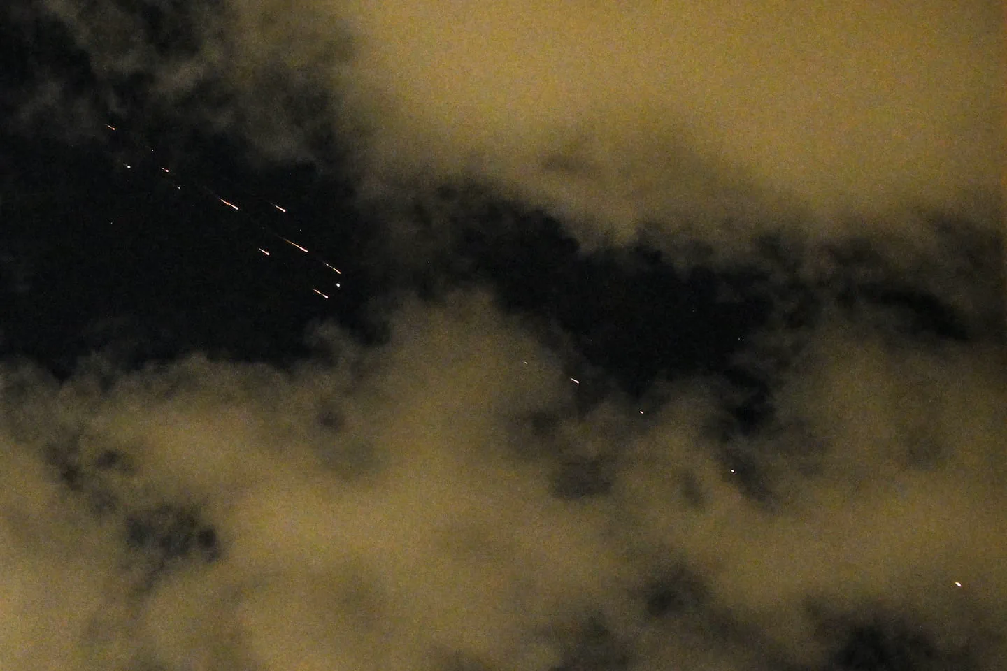 Múltiples luces brillantes y estelas cruzando un cielo nocturno con nubes.