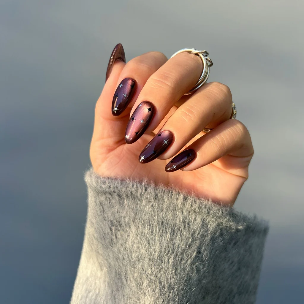 Una mano con anillos y sweater gris luce unas largas con un diseno de estrellas sobre fondo marron.