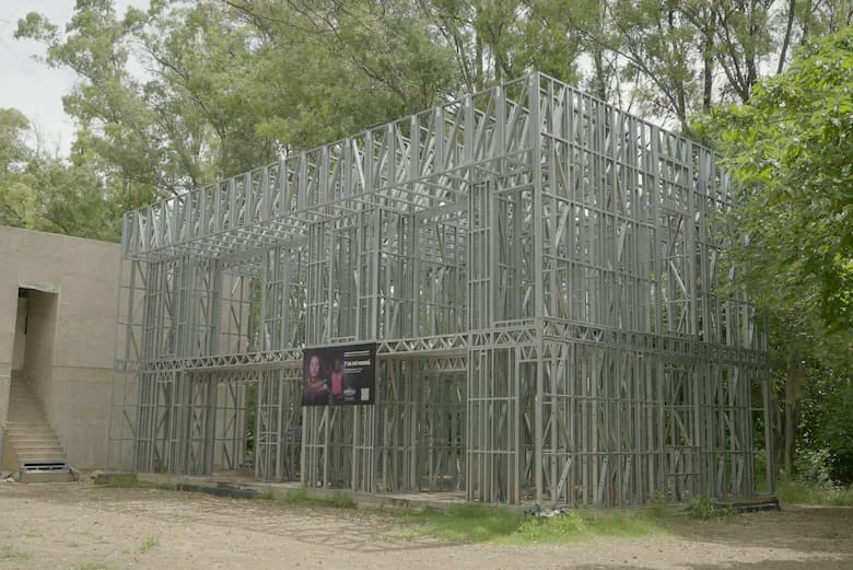 La estructura metálica de una casa en construcción se alza frente a una arboleda espesa.