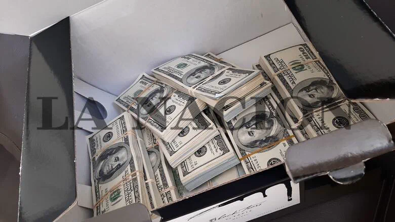 Varios fajos de billetes de cien dólares atados con gomitas elásticas adentro de una caja abierta.