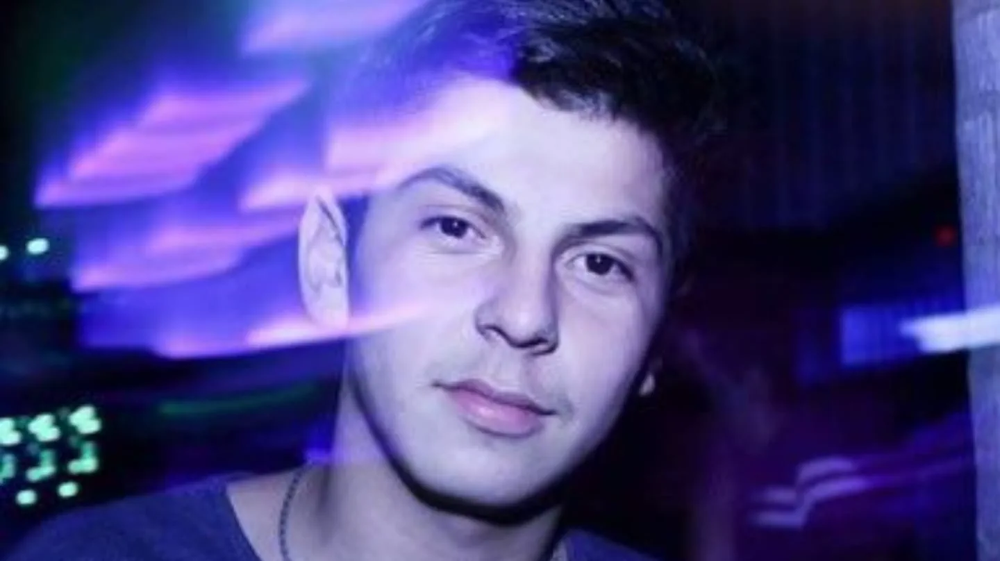 Un joven mira hacia adelante iluminado con luces violáceas en un boliche o fiesta nocturna.