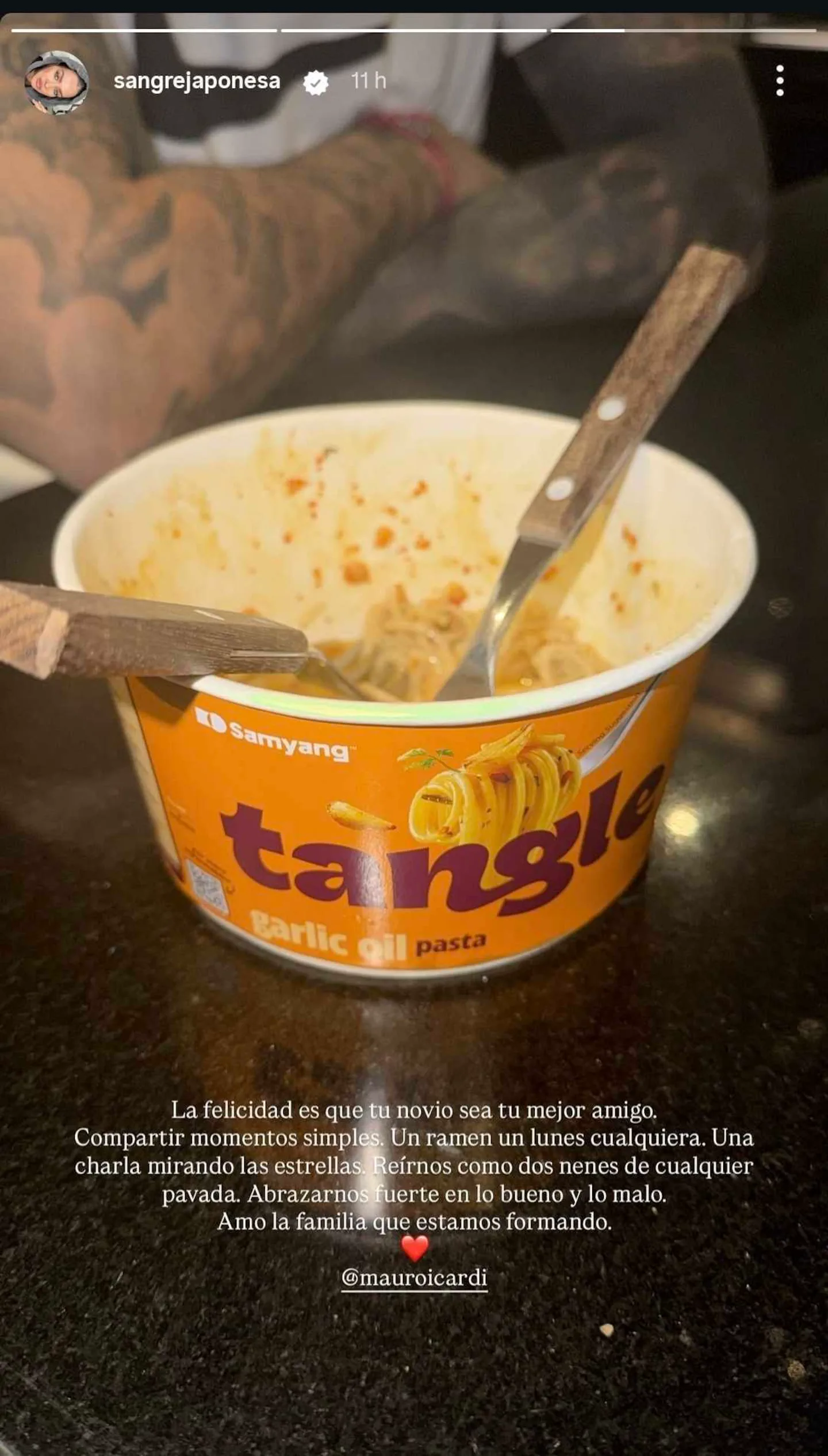 Un pote de fideos instantáneos con dos tenedores apoyados sobre una mesa negra.