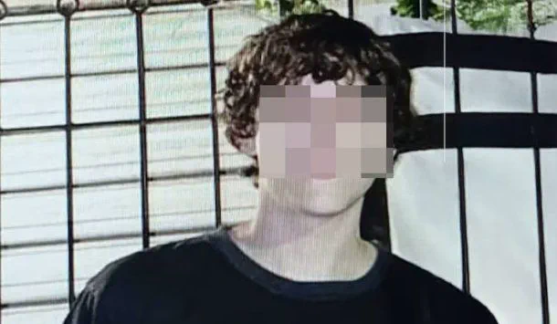 Un joven con remera negra y pelo ondulado tiene el rostro pixelado frente a una reja.