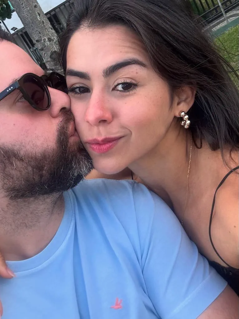 Un hombre de barba y anteojos de sol le da un beso en la mejilla a una mujer sonriente.
