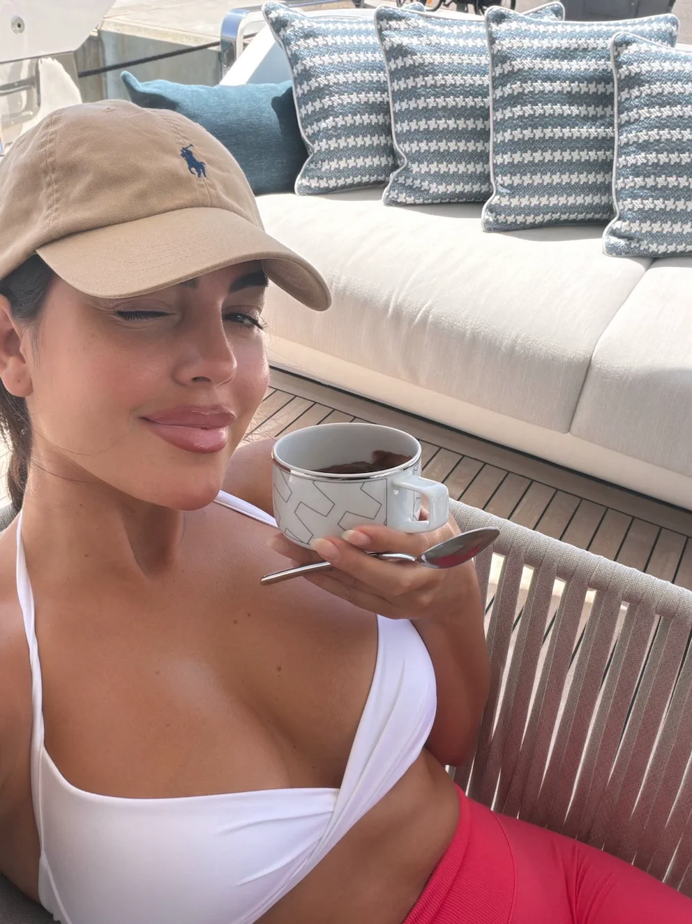 Georgina Rodríguez guiña un ojo mientras sostiene una taza blanca con una cuchara, sentada al aire libre.