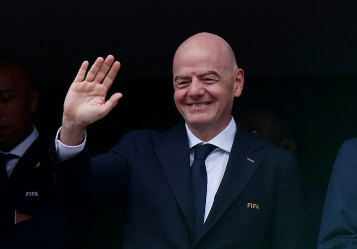 Gianni Infantino sonríe y saluda con la mano derecha levantada.