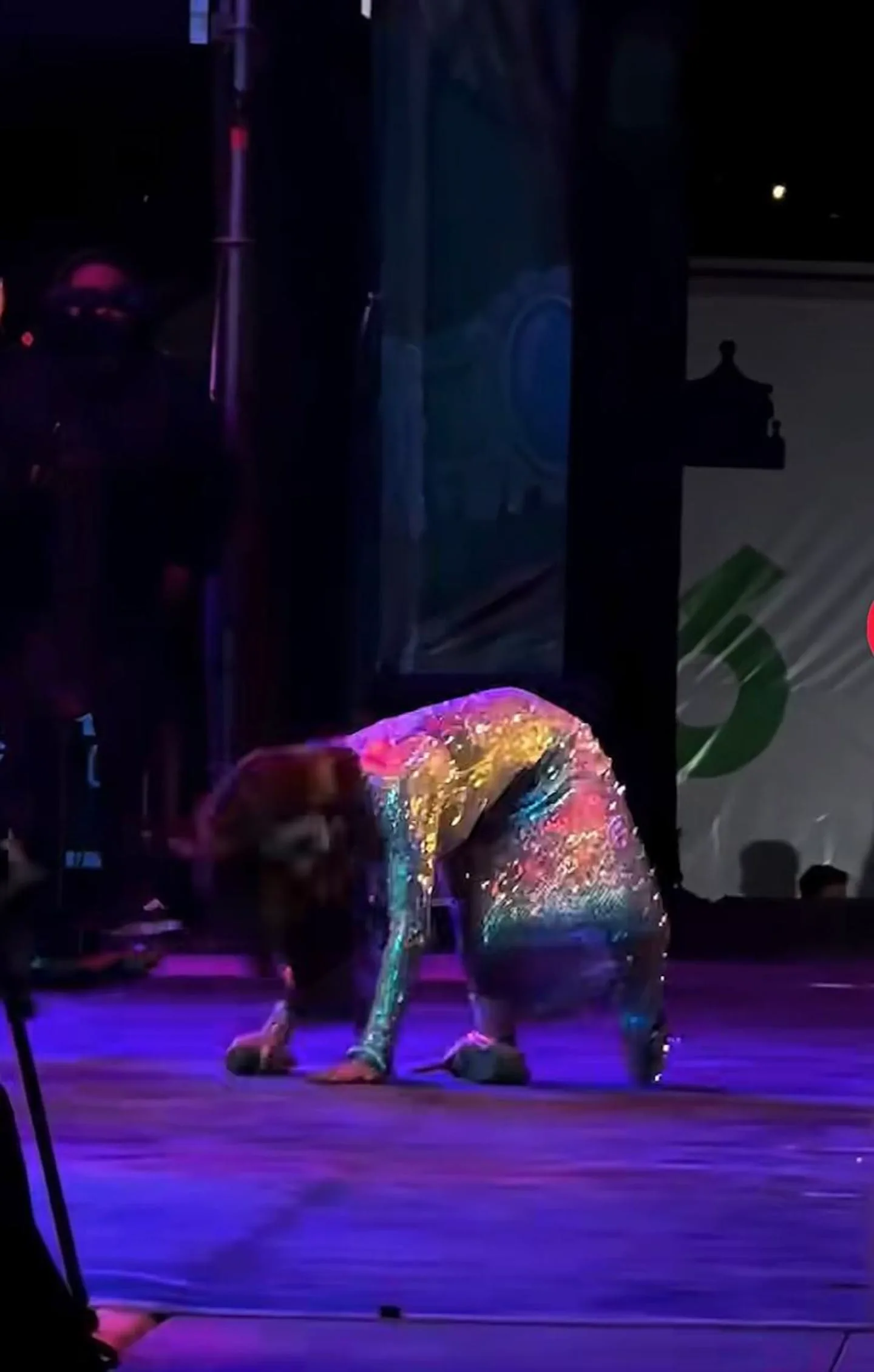 Una persona con vestido brillante arrodillada sobre un escenario iluminado durante un espectáculo.