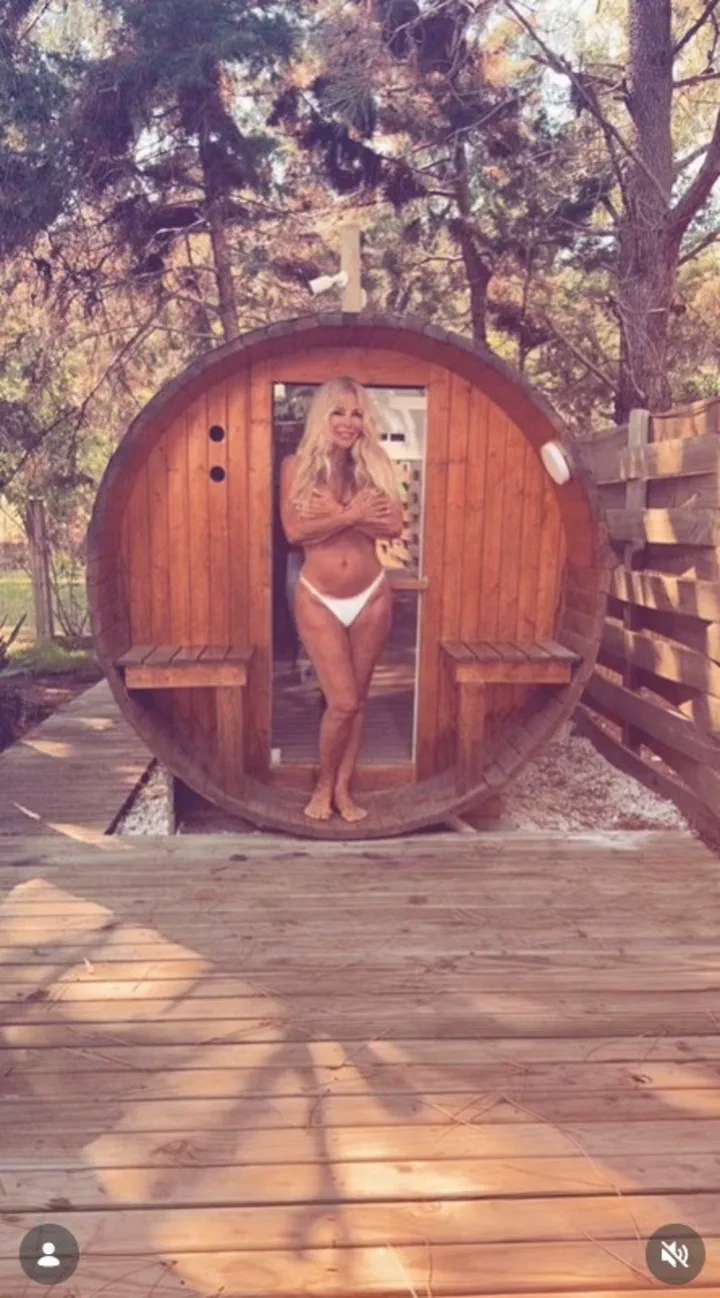 Graciela Alfano posa en la entrada de un sauna de madera con forma de barril en un entorno arbolado.
