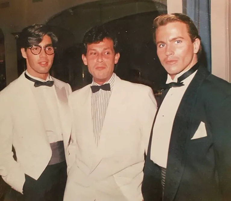 Tres hombres de traje y moño posan juntos en un evento nocturno.