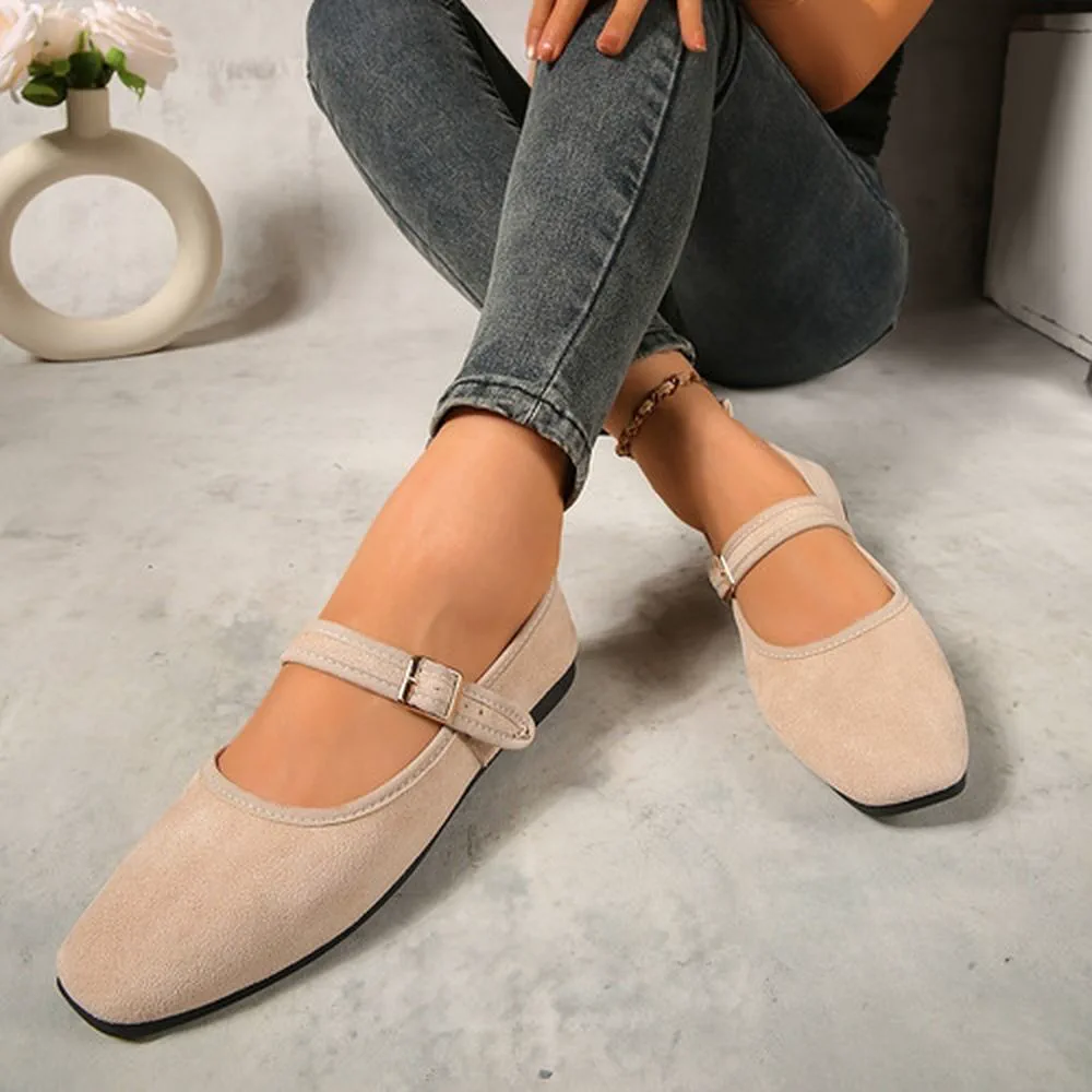 Una persona sentada en el suelo muestra zapatos chatos tipo guillermina en tono beige claro.