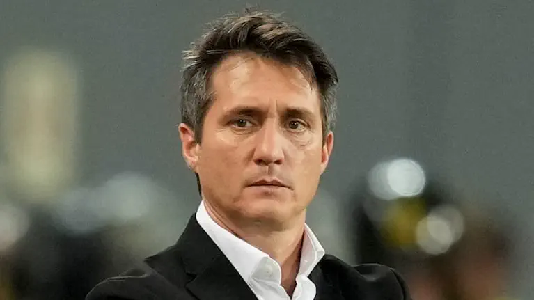 Guillermo Barros Schelotto mirando de frente con traje negro y camisa blanca.