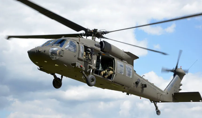 Un helicóptero militar de transporte en pleno vuelo lleva su compuerta lateral abierta con personal a bordo.
