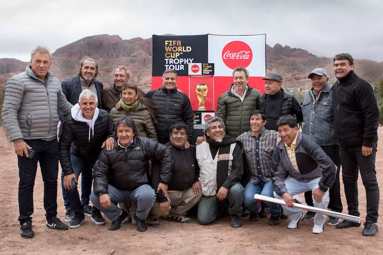 Un grupo de personas posa al aire libre junto a una réplica de la Copa del Mundo de fútbol.