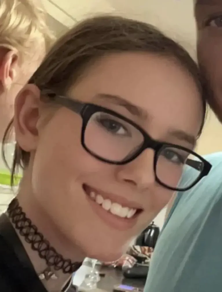 Primer plano de una joven sonriendo con anteojos de marco negro y gargantilla.