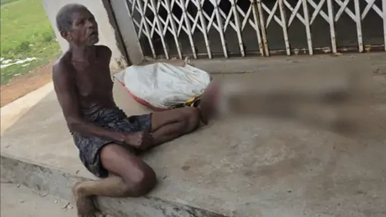 Un hombre con el torso desnudo esta sentado en el suelo de una galeria al aire libre.