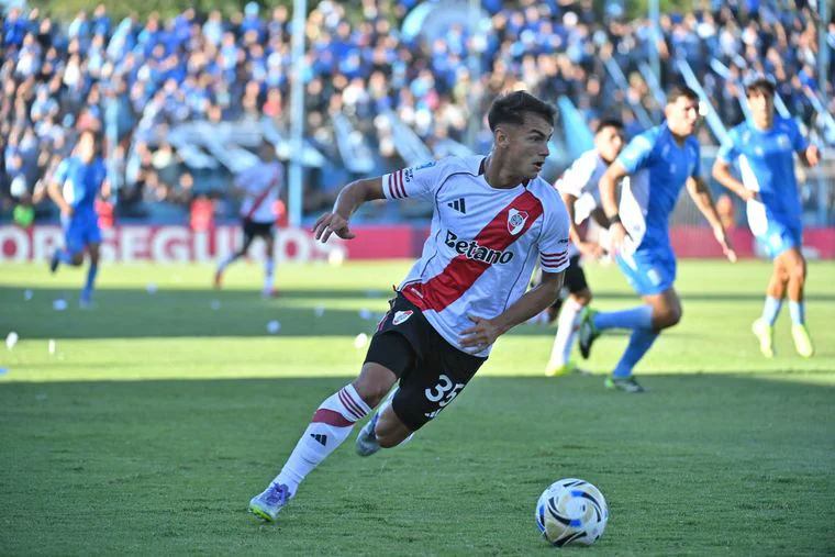 Un futbolista con la camiseta de River Plate corre con la pelota dominada sobre el pasto durante un partido.