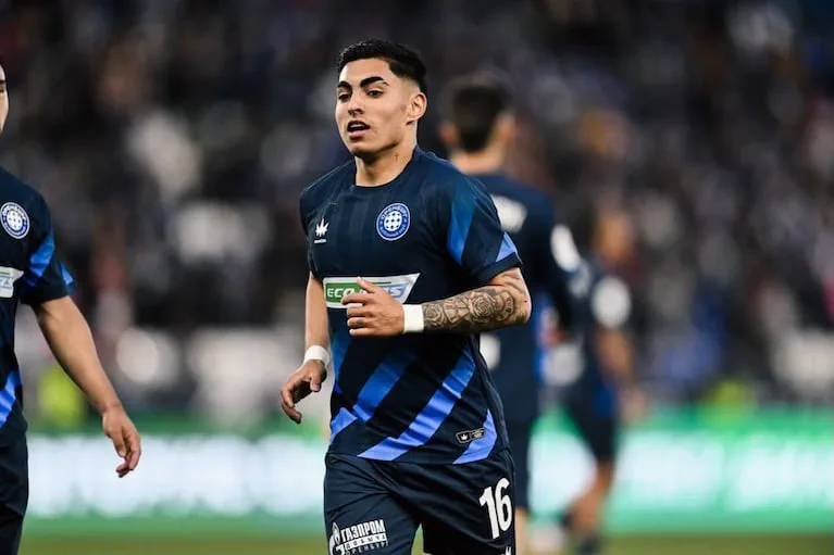 Un futbolista corre en la cancha vistiendo la camiseta azul con franjas del FC Oremburgo.
