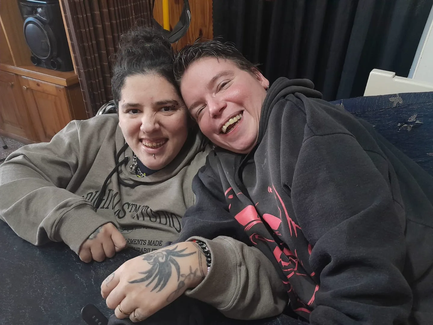 Dos personas con buzo con capucha sonríen abrazadas frente a una mesa.