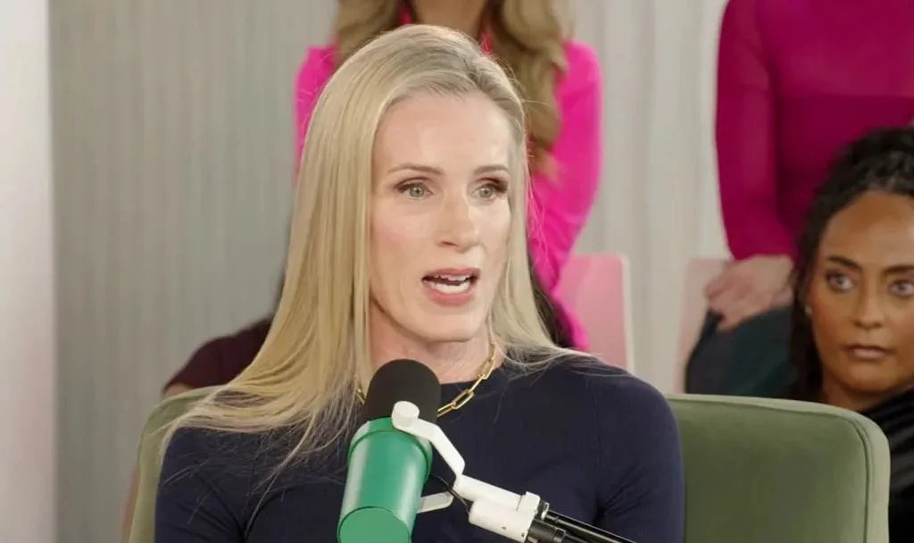Una mujer rubia con remera oscura habla frente a un micrófono verde en un estudio.
