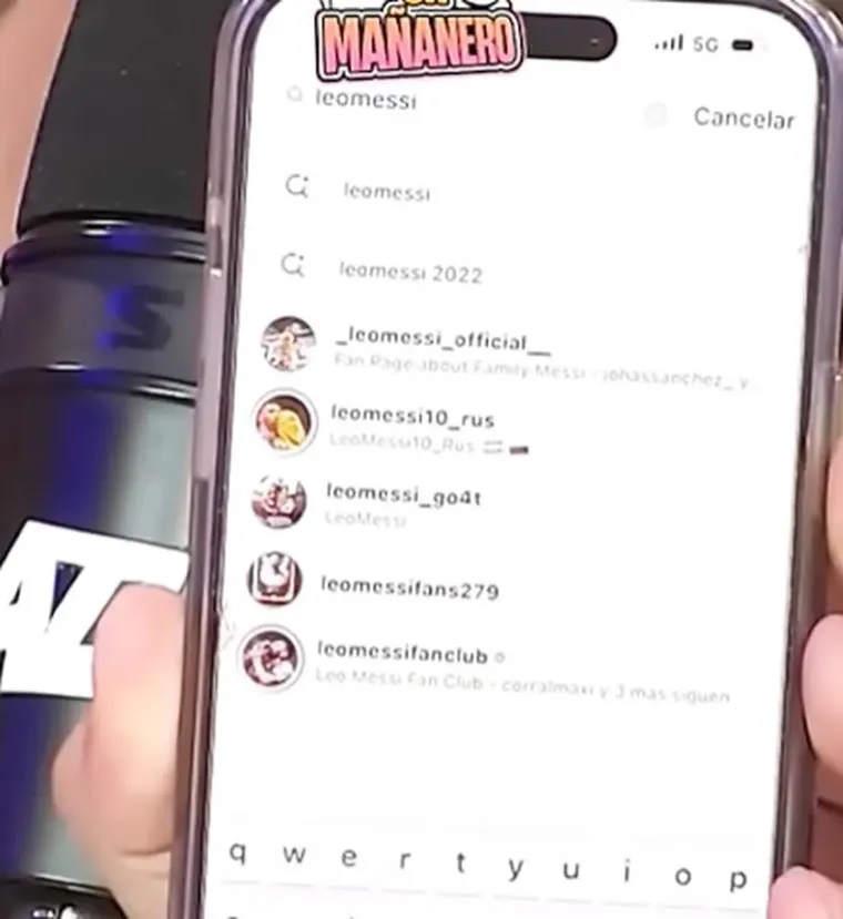 Una mano sosteniendo un celular que muestra la búsqueda de cuentas de Leo Messi en Instagram.