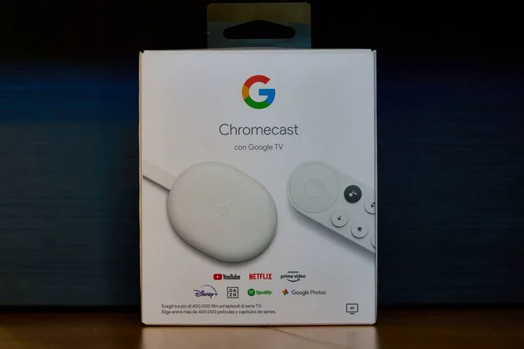 La caja blanca de un dispositivo Chromecast con Google TV y su control remoto sobre una superficie de madera.