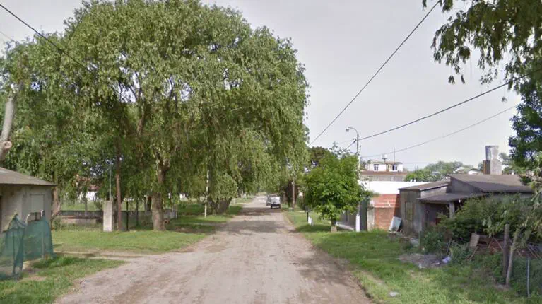 Una calle de tierra arbolada con casas bajas a los costados y un vehiculo al fondo.
