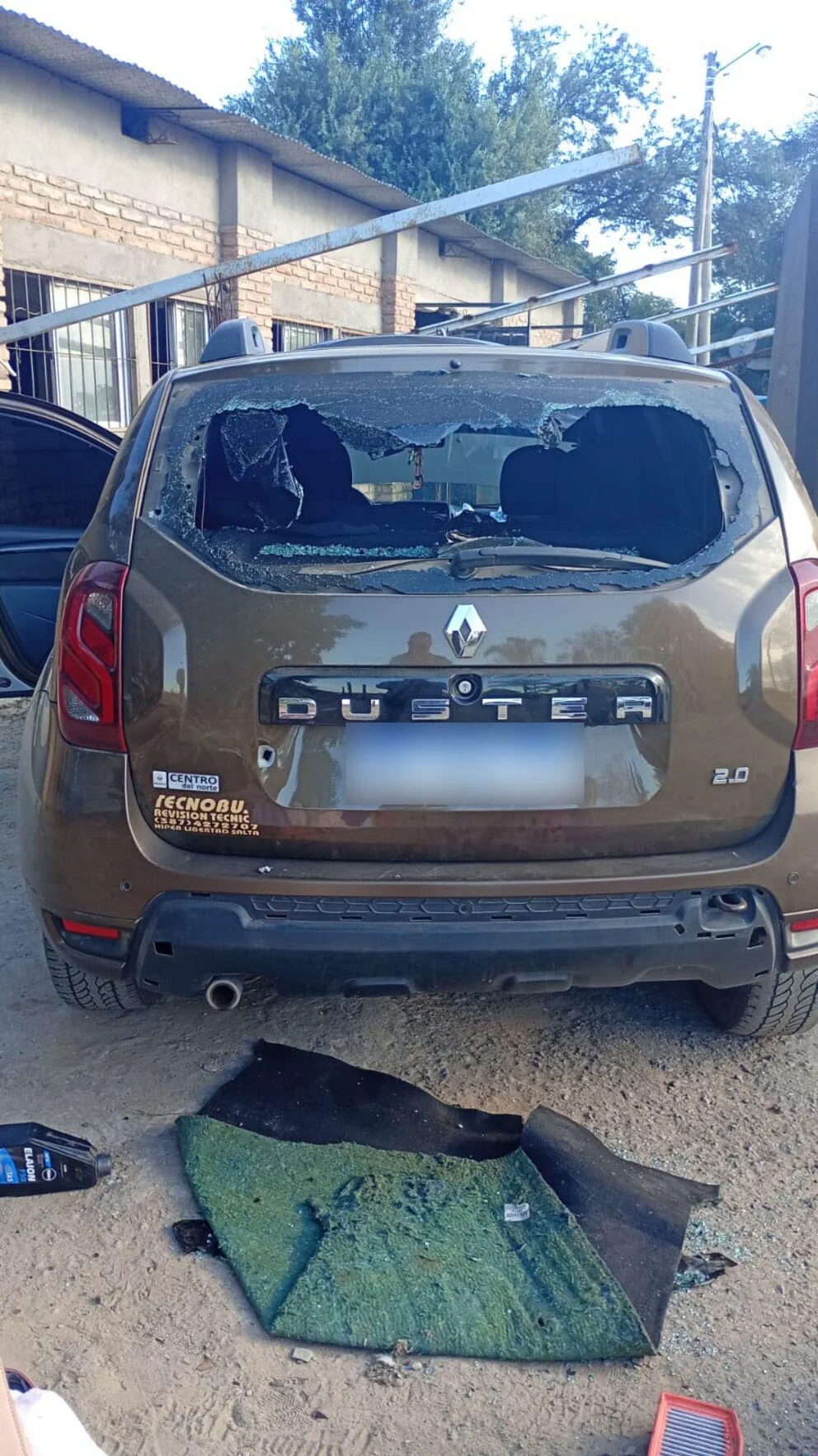 Una camioneta Renault Duster marrón tiene la luneta trasera destrozada y una alfombra tirada en el suelo.