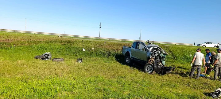 Una camioneta plateada con el frente chocado permanece detenida en la banquina con varias personas alrededor.