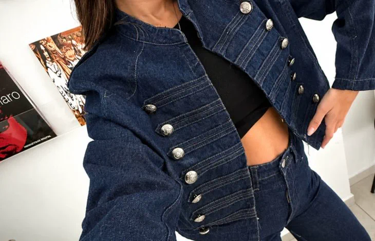Una persona viste una campera de jean oscuro con botones metálicos y un top negro.