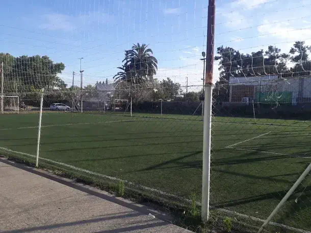 Una cancha de futbol de cesped sintetico se ve detras de una red de contencion en un dia despejado.
