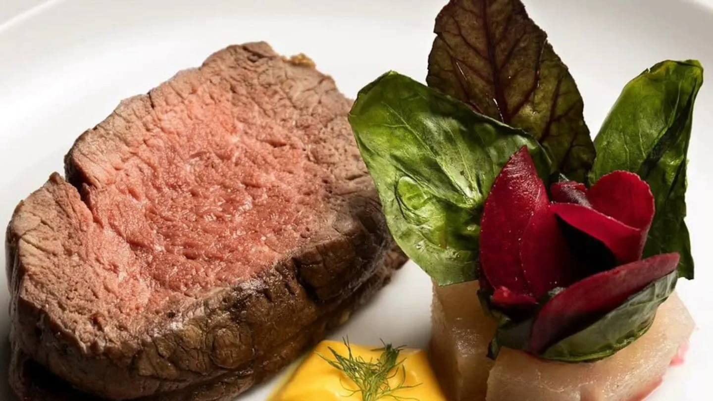 Un bife de carne vacuna cocido acompañado por vegetales sobre un plato blanco.