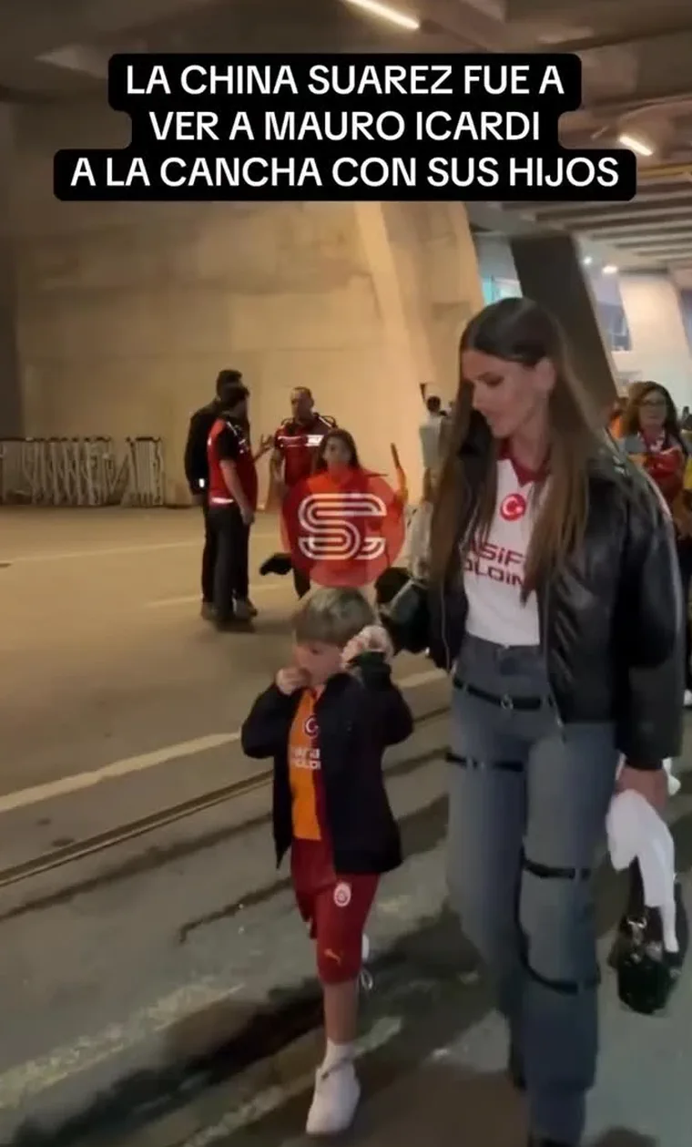 Una mujer camina de la mano con un nene vestido con ropa de fútbol en un playón.