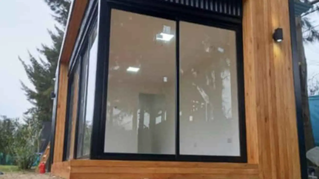Una construccion modular revestida en madera clara con un gran ventanal corredizo de marco negro.