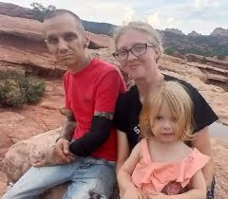 Un hombre, una mujer con anteojos y una nena están sentados al aire libre en una zona rocosa.