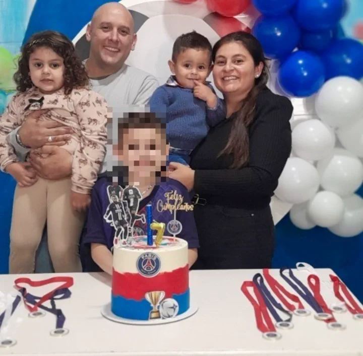 Una familia festeja un cumpleanos infantil posando detras de una torta con decoracion de futbol y medallas en la mesa.