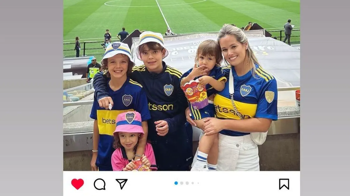 Una mujer y cuatro chicos con indumentaria y pilusos de Boca Juniors posan sonrientes en una tribuna de la cancha.