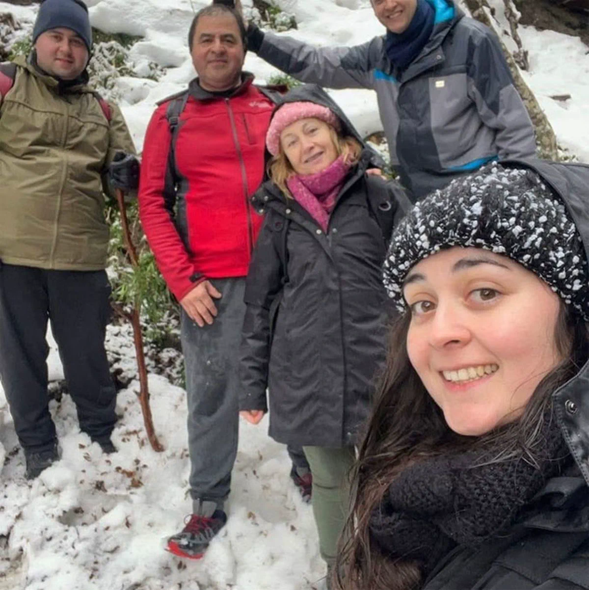 Un grupo de personas posa sonriendo abrigadas en un bosque cubierto de nieve.