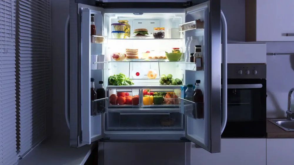 Una heladera con las dos puertas abiertas llena de frutas, verduras, botellas y alimentos iluminados.