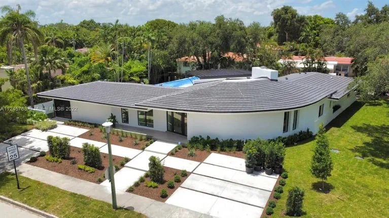Vista aerea de una casa moderna de una planta pintada de blanco con techo gris y cesped alrededor.