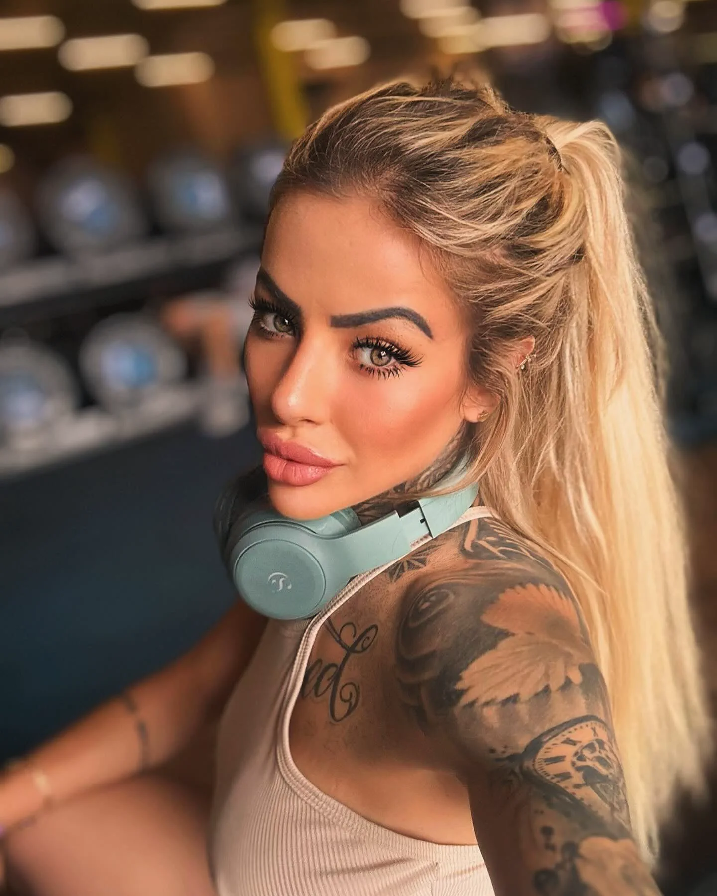 Una mujer rubia con tatuajes y auriculares alrededor del cuello posa mirando a la cámara.