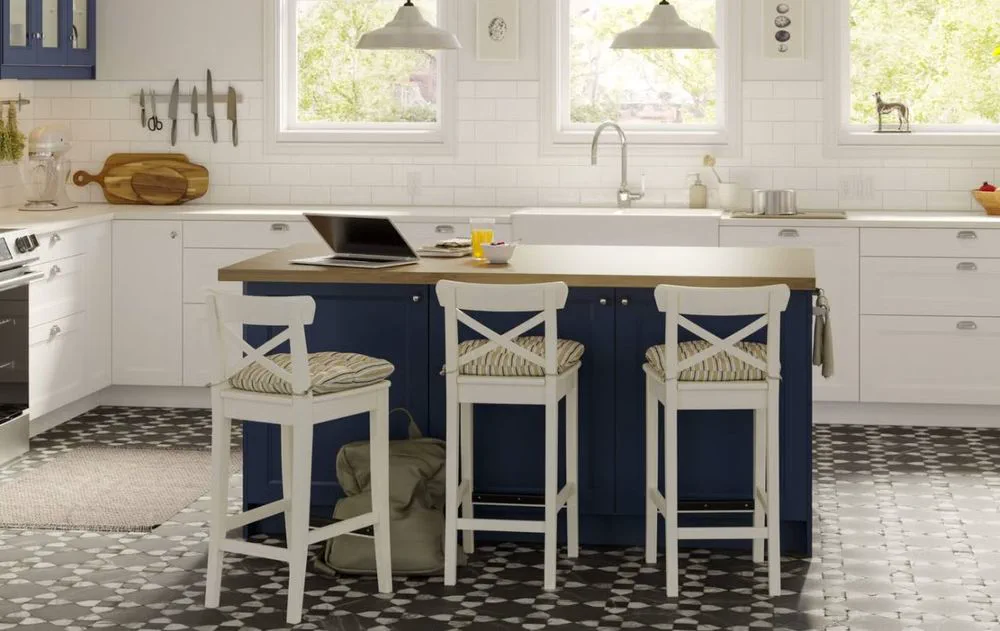 Una cocina con isla azul, mesada de madera, tres banquetas blancas y una notebook abierta.