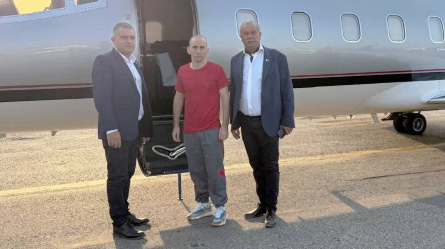 Tres hombres posan de pie en la pista junto a las escalerillas de un avión privado.