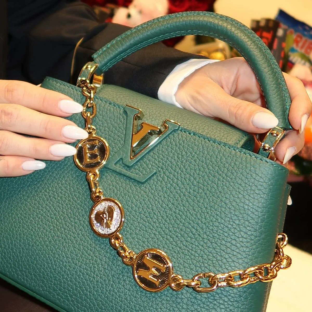Una persona sostiene con ambas manos una cartera de cuero verde con detalles dorados de Louis Vuitton.
