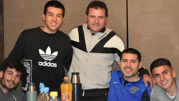 Cinco hombres posan sonriendo alrededor de una mesa con termos y bebidas.